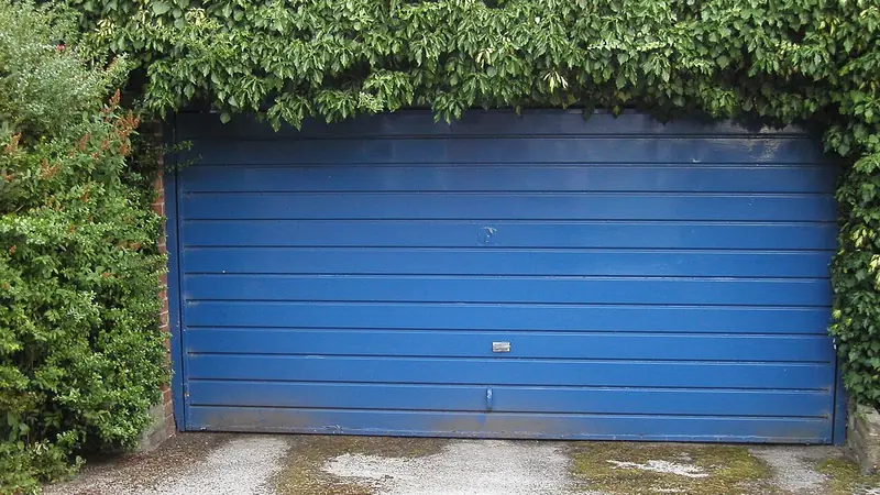 Blaues Schwingtor einer Garage zwischen Hecken